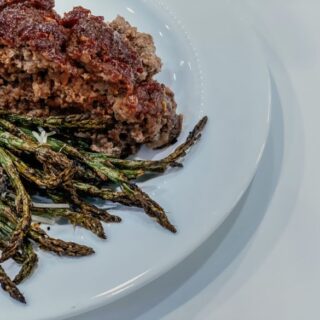 Meatloaf on a white plate with asparagus.