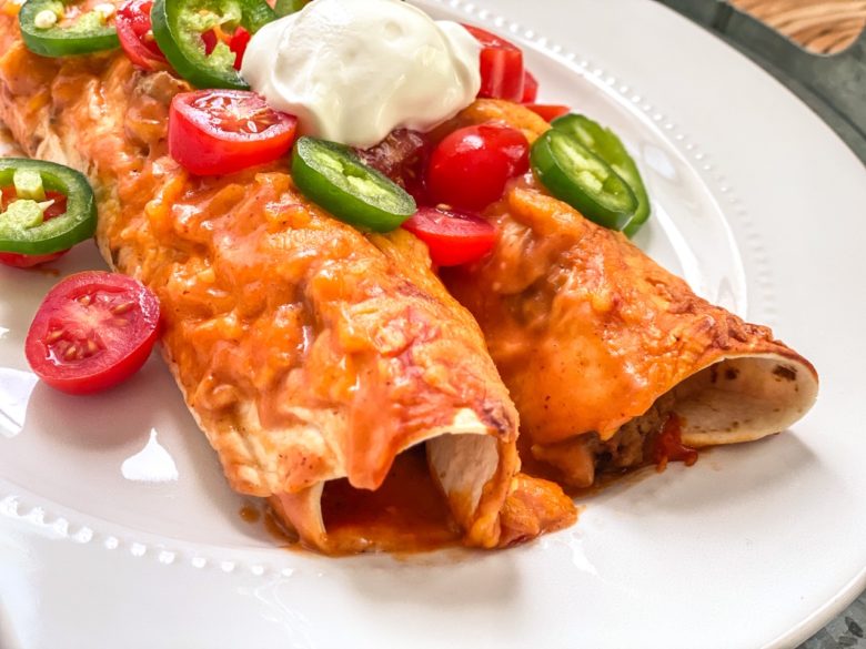 Cheesy enchiladas on a plate with tomatoes, jalapeno, and sour cream. 