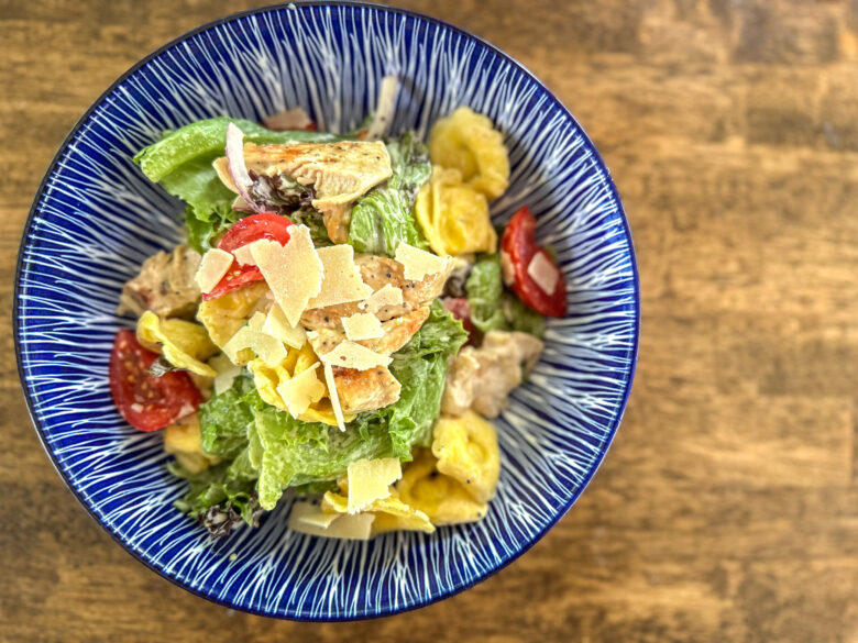 Caesar salad with cold tortellini pasta and parmesean cheese.